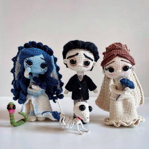 Peut inclure: Poupées crochetées inspirées d'un film, représentant une mariée à la peau bleue avec des cheveux bleu foncé, un marié en costume noir et une mariée en robe blanche. Un serpent vert et un chien squelette sont également inclus. Fait à la main.