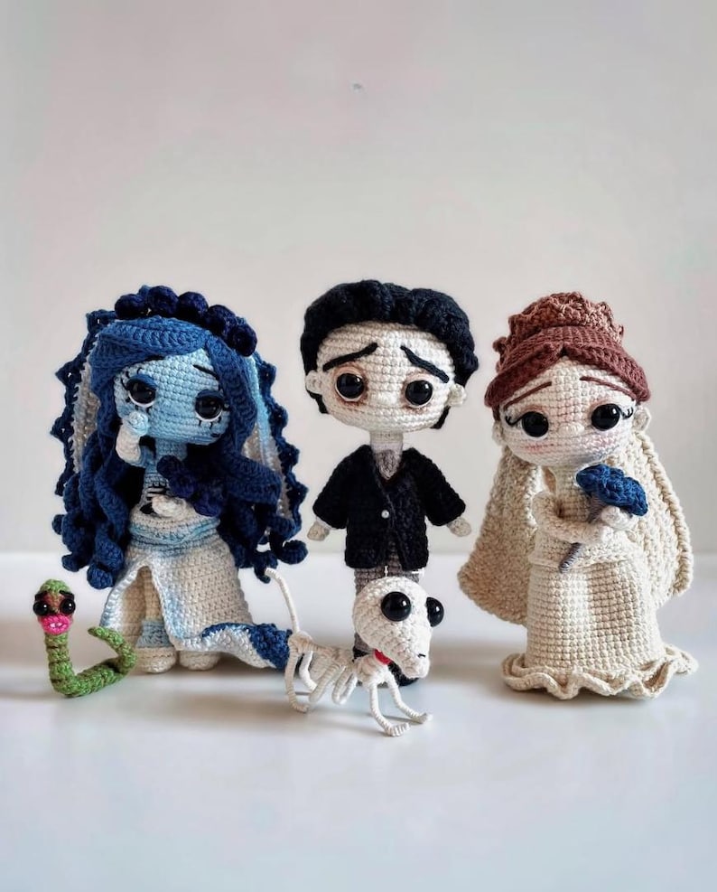 Puede incluir: Mu&ntilde;ecos de ganchillo inspirados en una pel&iacute;cula, con una novia de piel azul con cabello azul oscuro, un novio con traje negro y una novia con vestido blanco. Tambi&eacute;n se incluye una serpiente verde y un perro esqueleto. Hecho a mano.