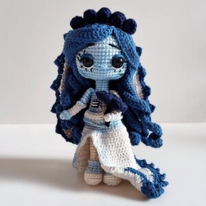 Puede incluir: Mu&ntilde;eca de ganchillo hecha a mano en tonos azules y blancos. La mu&ntilde;eca tiene grandes ojos negros, pelo azul y un vestido blanco y azul. La mu&ntilde;eca es una representaci&oacute;n caprichosa de un personaje.