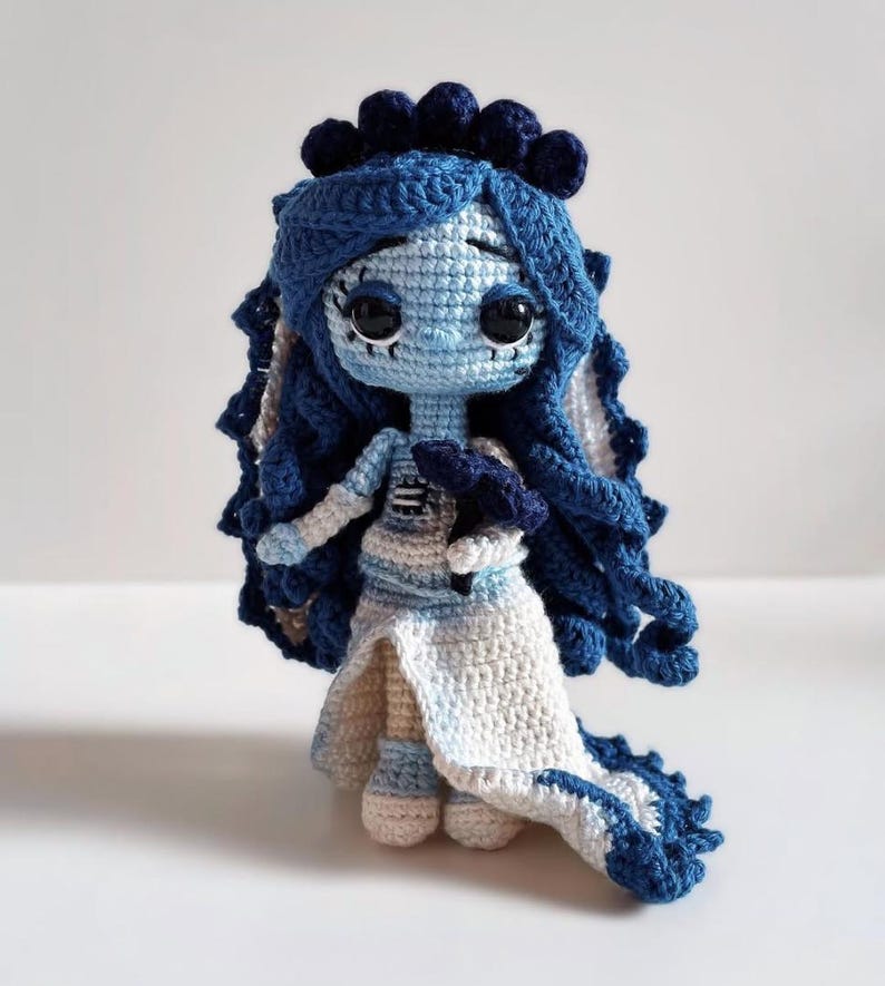 Puede incluir: Mu&ntilde;eca de ganchillo hecha a mano en tonos azules y blancos. La mu&ntilde;eca tiene grandes ojos negros, pelo azul y un vestido blanco y azul. La mu&ntilde;eca es una representaci&oacute;n caprichosa de un personaje.