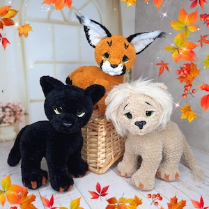 May include: Three crocheted animal toys: a black panther, an orange fox, and a tan lion. The toys have detailed features, including expressive eyes and soft textures. The fox and lion are sitting on a wicker basket.