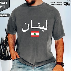 May include: A gray t-shirt with the Arabic word "Lebanon" in white, along with the Lebanese flag. The shirt has the words "Super Soft" and "Pepper" on the upper left corner.