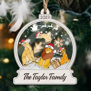 May include: A wooden Christmas ornament shaped like a snow globe, featuring a lion family wearing Santa hats. The ornament has the year 2023 at the top and the text "The Taylor Family" at the bottom. Inside the globe are snowflakes and a reindeer sleigh.