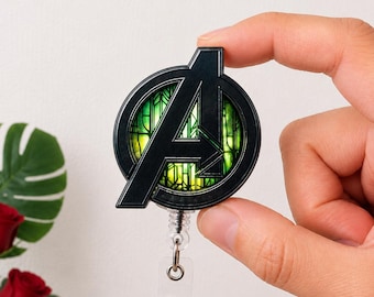 Può includere: Un portabadge circolare con l'emblema nero del logo Avengers su uno sfondo in stile vetrata colorata verde e giallo. L'emblema è fissato a un cinturino in plastica trasparente con una chiusura a bottone in metallo per le carte d'identità.