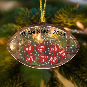 May include: A football-shaped wooden ornament with a gold hanging cord. The centre features a star-patterned background with the text TEAM NAME 2024 and six red football helmets, each personalised with a name and a two-digit number.