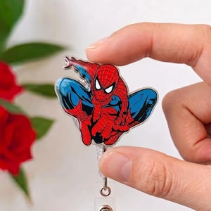 May include: A retractable badge reel featuring a colorful graphic of the comic book character Spider-Man in a crouching pose. The character is depicted in a red and blue suit with black web patterns, attached to a clear plastic reel mechanism.