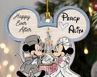 May include: A Mickey Mouse-shaped wooden ornament featuring a bride and groom illustration, a castle graphic, and the text "Happy Ever After" and "Percy Alita" with a blue heart. The ornament is suspended by a gold string against a tree.