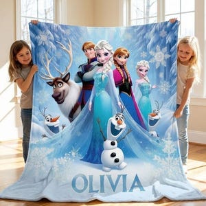 May include: A light blue blanket featuring characters from the animated film Frozen, including Elsa, Anna, Olaf, and Kristoff, set against a snowy forest backdrop. The name "OLIVIA" is printed at the bottom in white letters.