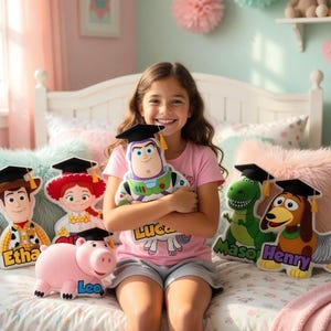 May include: A young girl smiles, holding a Buzz Lightyear plush toy. Other Toy Story character plushies, including Woody, Jessie, Rex, Slinky Dog, and Hamm, are arranged on a bed. Each character wears a graduation cap.