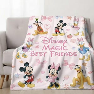 Puede incluir: Una manta rosa claro de Disney Magic Best Friends con Mickey Mouse, Minnie Mouse, Donald Duck, Daisy Duck, Goofy y Pluto. La manta tiene lazos y estrellas rosas esparcidos por la superficie.