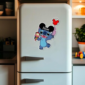 May include: A blue cartoon character sticker with the word "Name" on a black hat, holding an ice cream cone and a red balloon. The sticker is affixed to a white refrigerator door.