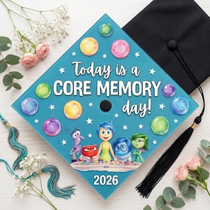 May include: A graduation cap with a teal blue top decorated with colorful circles and stars. The text "Today is a CORE MEMORY day!" is displayed, along with the year "2026" and characters from the movie Inside Out. A black tassel hangs from the cap.
