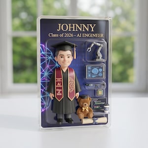 May include: A clear display case with a graduation figurine of a person in a cap and gown, with the name "JOHNNY" and "Class of 2026 - AI ENGINEER" printed at the top. The case includes a teddy bear, a robotic arm, and other AI-related elements.