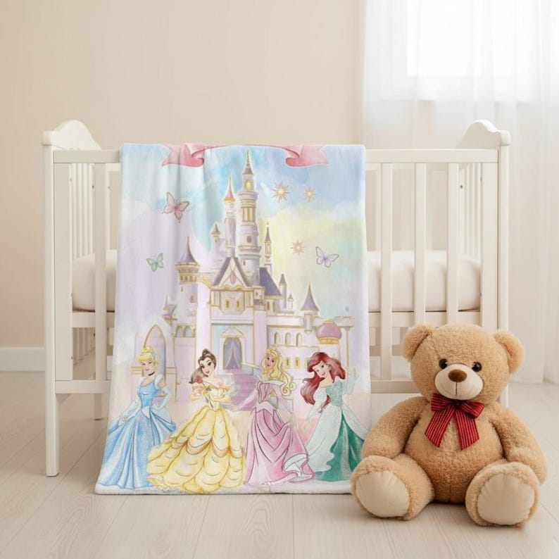 K&ouml;nnte beinhalten: Eine Babydecke mit einer Aquarellillustration eines Schlosses und Prinzessinnen in Kleidern. Die Decke ist &uuml;ber ein wei&szlig;es Kinderbett drapiert, mit einem Teddyb&auml;ren daneben. Die Decke hat ein hellblaues, rosa und gelbes Farbschema.