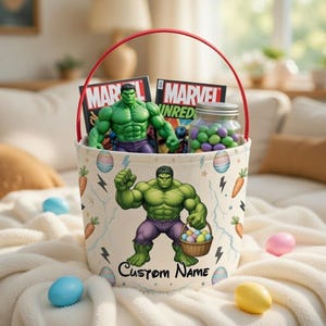 May include: A white Easter basket with a red handle, featuring a Hulk graphic and the text "Custom Name." The basket contains a Hulk figurine, comic books, and a jar of candy. Easter eggs are scattered around the basket.