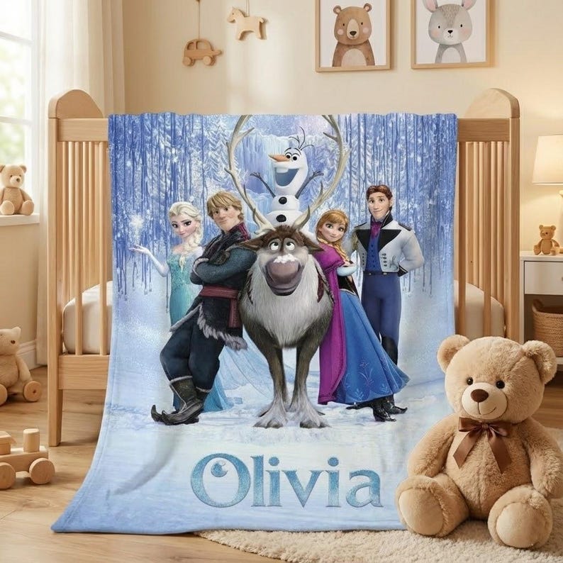 Puede incluir: Una manta azul claro con personajes de la pel&iacute;cula animada Frozen, incluyendo a Elsa, Anna, Kristoff, Olaf y Sven. La manta tiene un fondo de bosque invernal y el nombre "Olivia" en escritura azul claro.