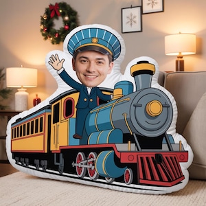 Op de afbeelding: Een op maat gevormd sierkussen met een cartoonillustratie van een treinconducteur met een fotografisch gezicht, gekleed in een blauw uniform en pet, zwaaiend vanaf de bovenkant van een kleurrijke stoomlocomotief.