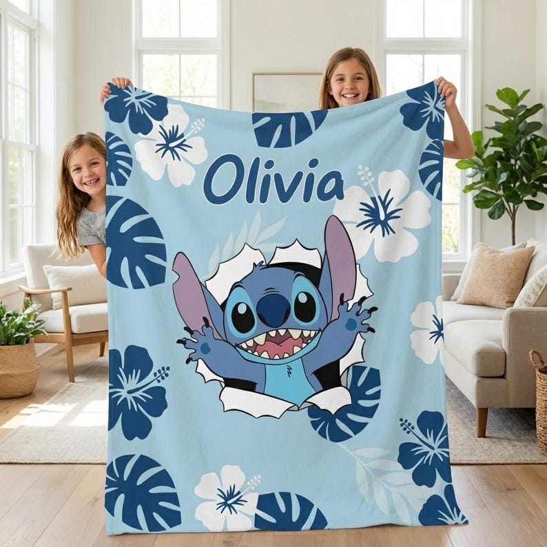 May include: A light blue blanket featuring the character Stitch bursting through a torn hole. The blanket is decorated with white and blue hibiscus flowers and the name "Olivia" in dark blue lettering. The blanket is held up by two people.