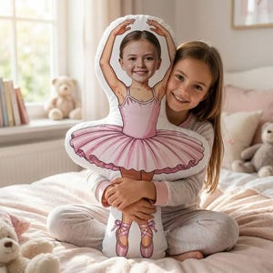 May include: A custom-shaped throw pillow featuring a printed illustration of a young ballerina in a pink tutu and ballet slippers. The pillow incorporates a photographic portrait of a child's face onto the illustrated dancer's head.