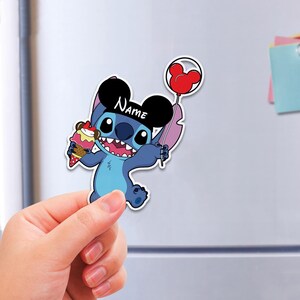 May include: A blue cartoon character sticker, holding an ice cream cone and a red Mickey Mouse balloon. The character wears a black hat with the word "Name" on it. The sticker is held up against a white background.