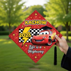 May include: Red glitter graduation cap featuring Lightning McQueen from the movie Cars. The cap has the text "KACHOW", "2026", and "Life is a Highway". Gold stars and a black tassel complete the design.