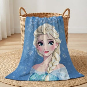 Pode incluir: Cobertor de l&atilde; polar azul com um retrato de personagem de desenho animado. A personagem tem cabelo loiro em uma tran&ccedil;a, olhos azuis e l&aacute;bios rosados. O nome "Olivia" est&aacute; escrito em branco no topo. O fundo &eacute; azul claro com flocos de neve brancos.