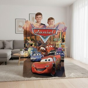 Puede incluir: Una manta de forro polar con personajes de la pel&iacute;cula Cars de Disney Pixar, con el nombre "daniel" impreso. La manta muestra a Rayo McQueen y otros coches en un entorno de ciudad des&eacute;rtica, con un fondo de puesta de sol.