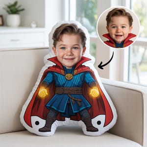 May include: A personalised cushion with a child's face on a cartoon superhero. The child is wearing a blue and red costume with glowing yellow hands. A smaller image of the child is in the upper right corner. The cushion is on a beige sofa.