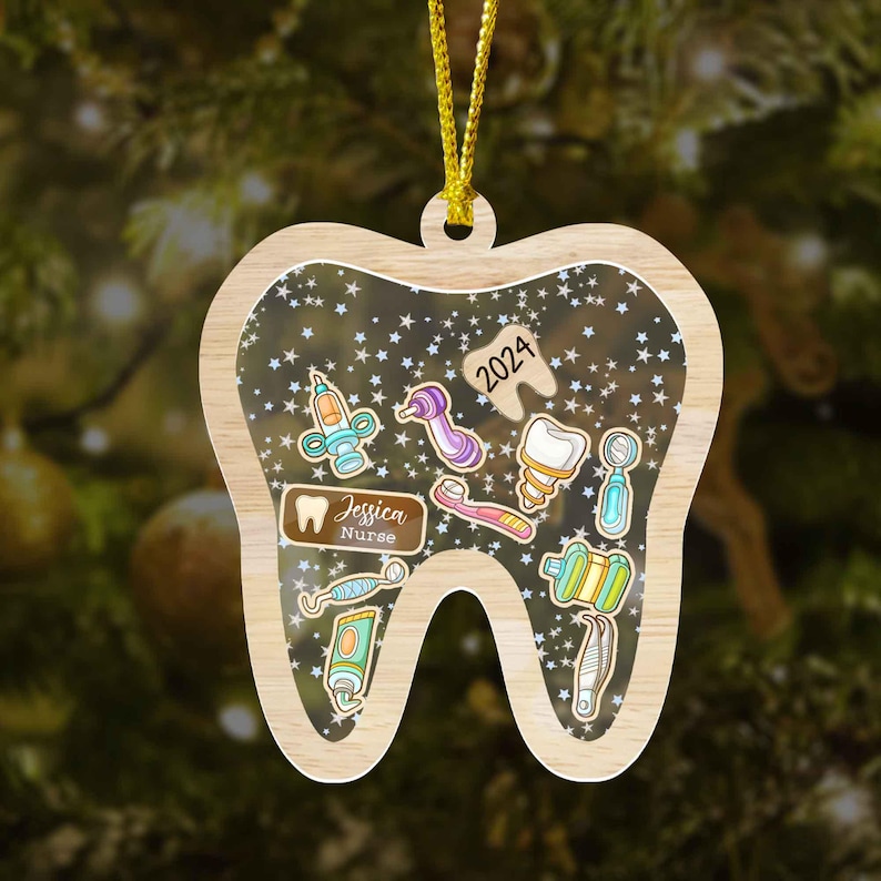 May include: Wooden tooth-shaped Christmas ornament with a clear center filled with dental tools and stars. The ornament includes the text "2024", a name, and the word "Nurse". The ornament hangs from a gold string.
