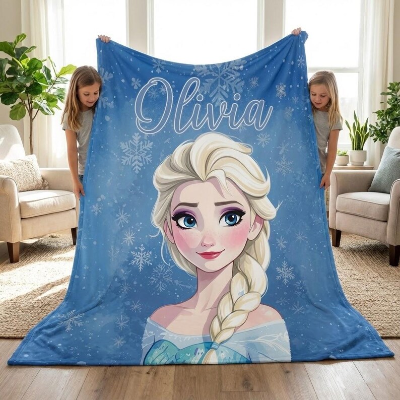 Pode incluir: Um cobertor de l&atilde; azul com uma ilustra&ccedil;&atilde;o de desenho animado de uma princesa com cabelo loiro e olhos azuis. O cobertor tem o nome "Olivia" em escrita branca e desenhos de flocos de neve. O cobertor &eacute; segurado por duas pessoas.