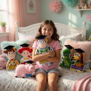 Puede incluir: Una ni&ntilde;a sonr&iacute;e mientras sostiene un peluche de Buzz Lightyear. Otros peluches de personajes incluyen a Woody, Jessie, Hamm, Rex y Slinky Dog, todos con gorros de graduaci&oacute;n. Los juguetes est&aacute;n sobre una cama con almohadas decorativas.