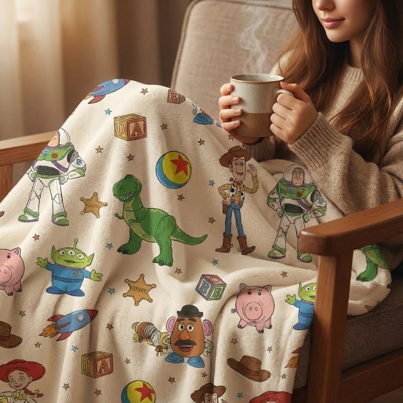 May include: A cream-colored blanket featuring cartoon characters from a popular animated film. The blanket has images of a green dinosaur, a space ranger, a cowboy, and other characters. The blanket is decorated with stars and other shapes.