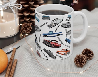 May include: White ceramic mug featuring a pattern of classic pickup trucks in various colors. The mug has the words "SQUAREBODY" and "SQUARE LIFE" printed on it. The mug is filled with a dark liquid.
