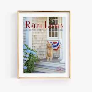 Puede incluir: Una impresión enmarcada que muestra un golden retriever en un porche con una pancarta roja, blanca y azul. La imagen incluye hortensias azules y el texto "RALPH LAUREN HOME COLLECTION AT THE POLO STORE". El marco es dorado.