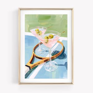 May include: A framed print featuring two pink martinis with olives, resting on a tennis racket. The background shows a tennis court with blue and green hues. The artwork has a retro, sporty theme.