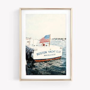 May include: A framed print featuring a white boat with the text "Boston Yacht Club Marblehead" in blue and red lettering. An American flag waves from the boat's mast. The boat is docked in the water, with black bumpers visible.
