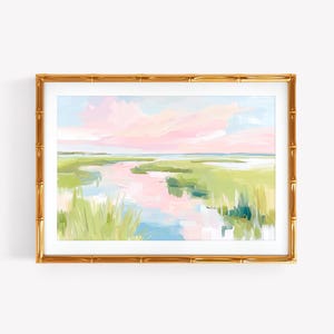 Op de afbeelding: Een landschapsschilderij in een gouden lijst in bamboestijl met een moeraslandschap met zachtroze wolken, lichtblauw water en felgroen gras. Het kunstwerk gebruikt losse penseelstreken om een serene kustwaterweg bij zonsondergang weer te geven.