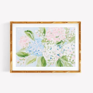 May include: A framed painting of hydrangea flowers in shades of light blue, soft pink, and white, accented with green leaves. The artwork is enclosed in a rectangular gold frame with a textured bamboo-style design, set against a plain background.