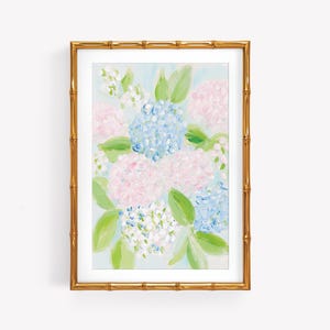 May include: A framed painting of hydrangea flowers in shades of light blue, soft pink, and white, accented with green leaves. The artwork is enclosed in a metallic gold frame with a textured bamboo-style design and a white mat border.
