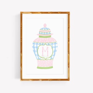 May include: A framed art print featuring a watercolor illustration of a ginger jar with a blue and white gingham pattern, pink accents, and a central white cartouche containing the letter M, enclosed in a gold bamboo-style frame.