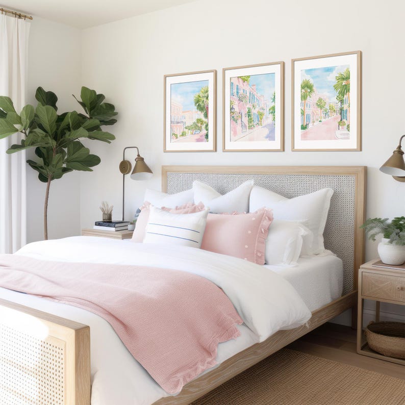 May include: A bedroom scene featuring a bed with a light wood frame and a woven headboard. The bed is dressed with white linens, pink pillows, and a pink throw blanket. Above the bed are three framed watercolor prints of a street scene.