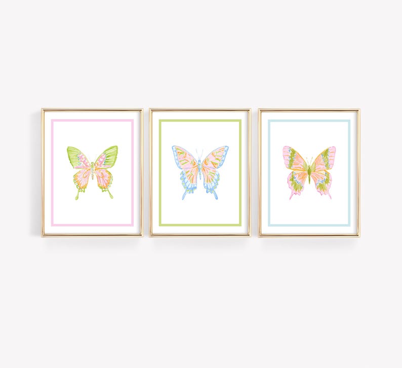 May include: Three framed butterfly art prints. Each print features a watercolor butterfly in shades of pink, green, and blue. The frames are gold, and the mats are pastel colors. The artwork is displayed on a white background.