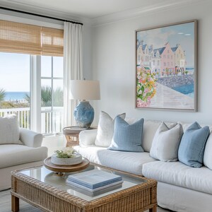 Puede incluir: Sal&oacute;n con sof&aacute; blanco, cojines azules y mesa de centro de mimbre. Un cuadro enmarcado de una escena costera cuelga de la pared. Una l&aacute;mpara de cer&aacute;mica azul sobre una mesa auxiliar. Ventanas grandes con vistas al mar.