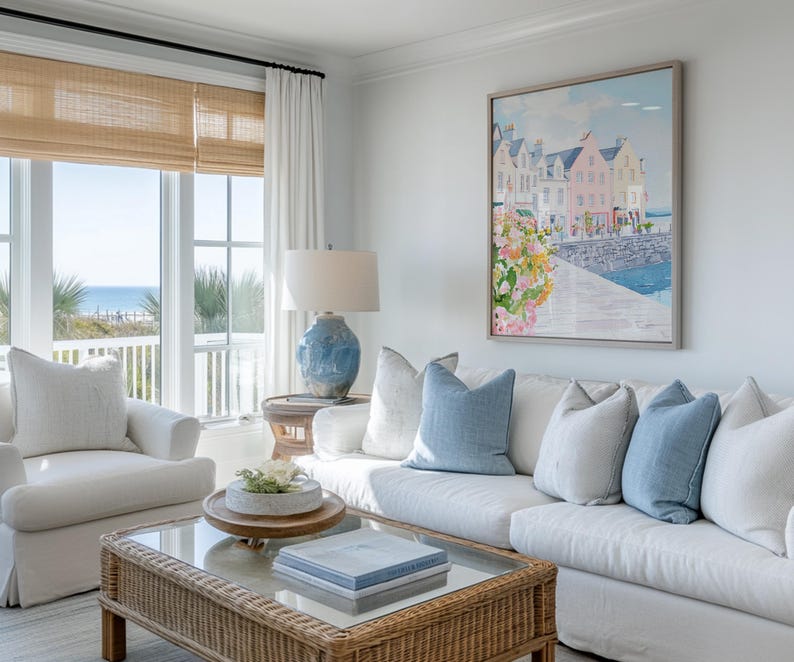 Puede incluir: Sal&oacute;n con sof&aacute; blanco, cojines azules y mesa de centro de mimbre. Un cuadro enmarcado de una escena costera cuelga de la pared. Una l&aacute;mpara de cer&aacute;mica azul sobre una mesa auxiliar. Ventanas grandes con vistas al mar.