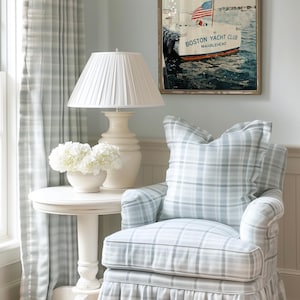 May include: A cozy living room scene featuring a plaid armchair, a small side table with a lamp, and a framed nautical print. The armchair and curtains have a blue and white plaid pattern. The print says "Boston Yacht Club, Marblehead."