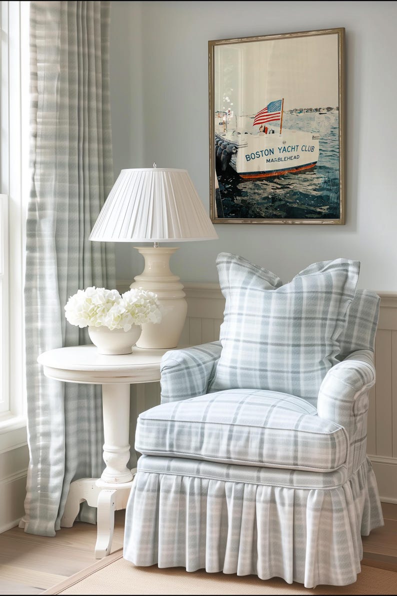 May include: A cozy living room scene featuring a plaid armchair, a small side table with a lamp, and a framed nautical print. The armchair and curtains have a blue and white plaid pattern. The print says "Boston Yacht Club, Marblehead."