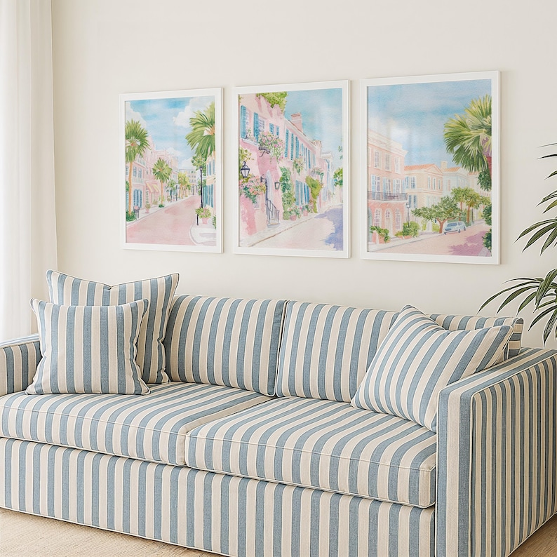 May include: A living room scene featuring a blue and white striped sofa with matching throw pillows. Above the sofa are three framed watercolor prints depicting a street scene with buildings and palm trees.