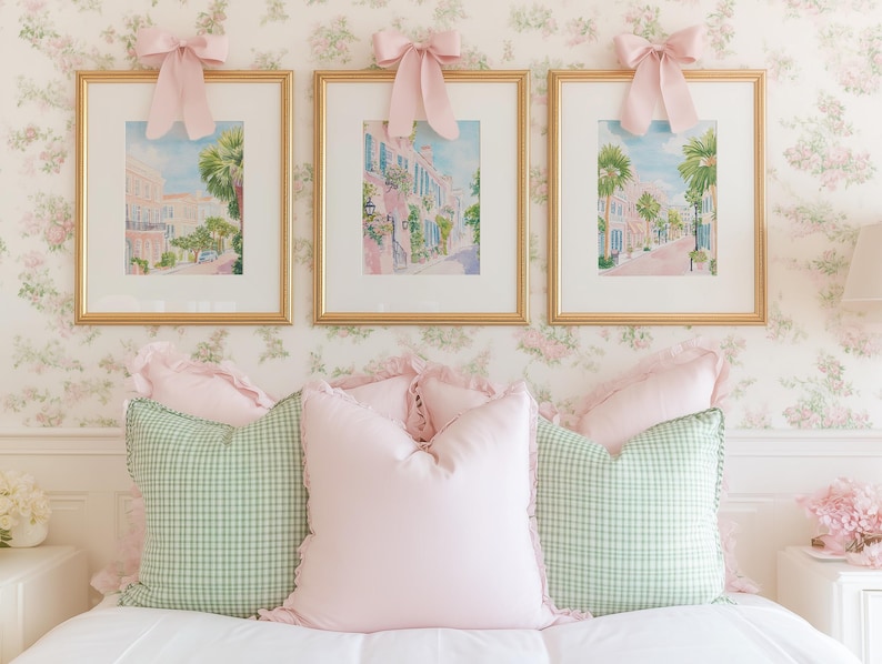 May include: Three framed watercolor prints of a street scene with pink buildings and palm trees, each topped with a pink bow. Below, a bed is adorned with pink and green gingham pillows, creating a soft, feminine aesthetic.