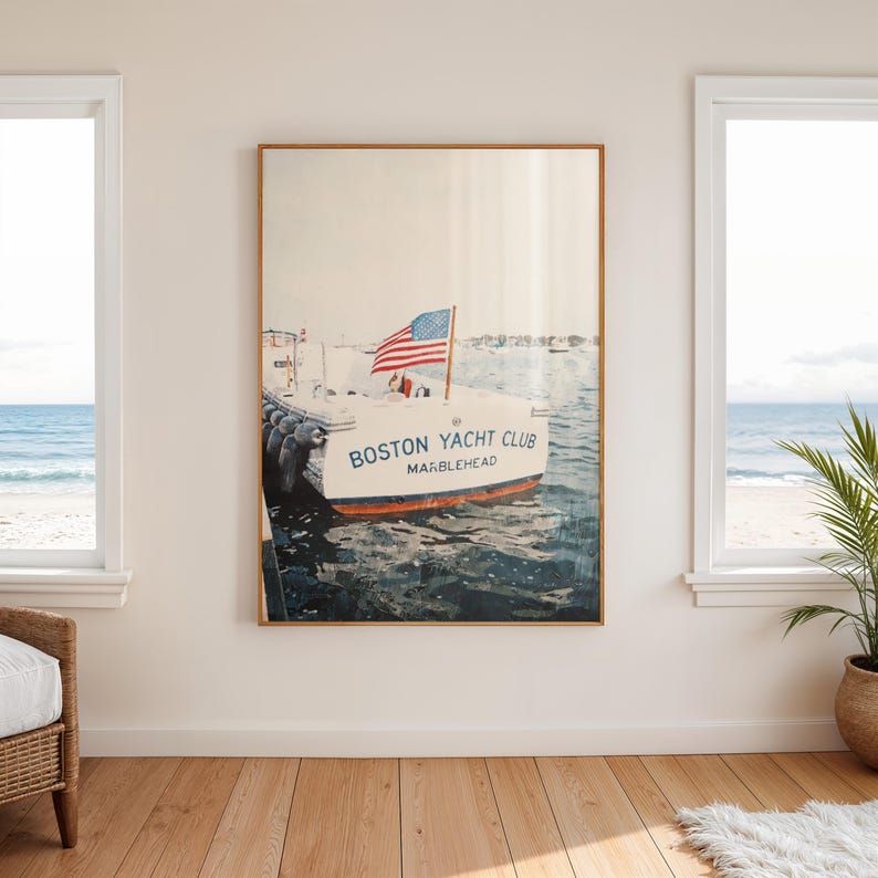 May include: A framed print featuring a boat with the text "BOSTON YACHT CLUB MARBLEHEAD" and an American flag. The boat is on the water, with a blue and white color scheme. The print is displayed in a room with windows overlooking the ocean.