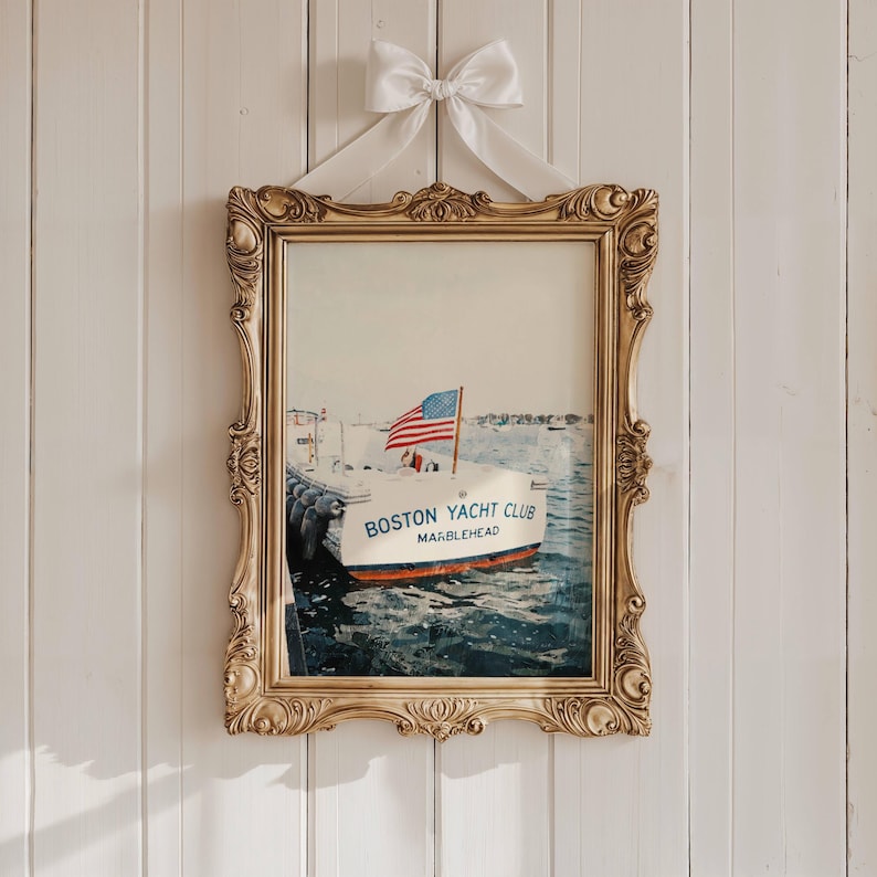 May include: A framed print of a boat with an American flag, labeled "BOSTON YACHT CLUB MARBLEHEAD." The print is in an ornate gold frame, suspended by a white bow against a white paneled wall. The boat is white with a red stripe.